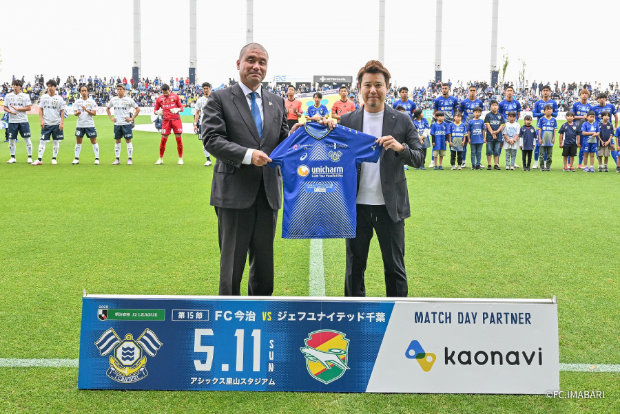 今治. 夢スポーツ代表取締役社長の矢野さんと、カオナビ表取締役社長の佐藤がFC今治のユニフォームを持って記念撮影をしている様子の写真